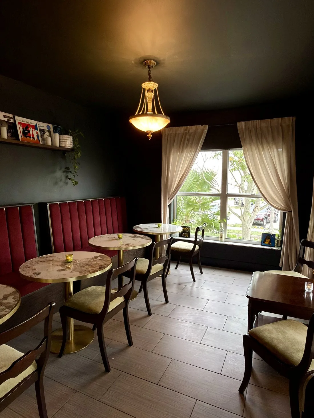 The café room — round marble tables along a red velvet banquette, with sunlight through the front window