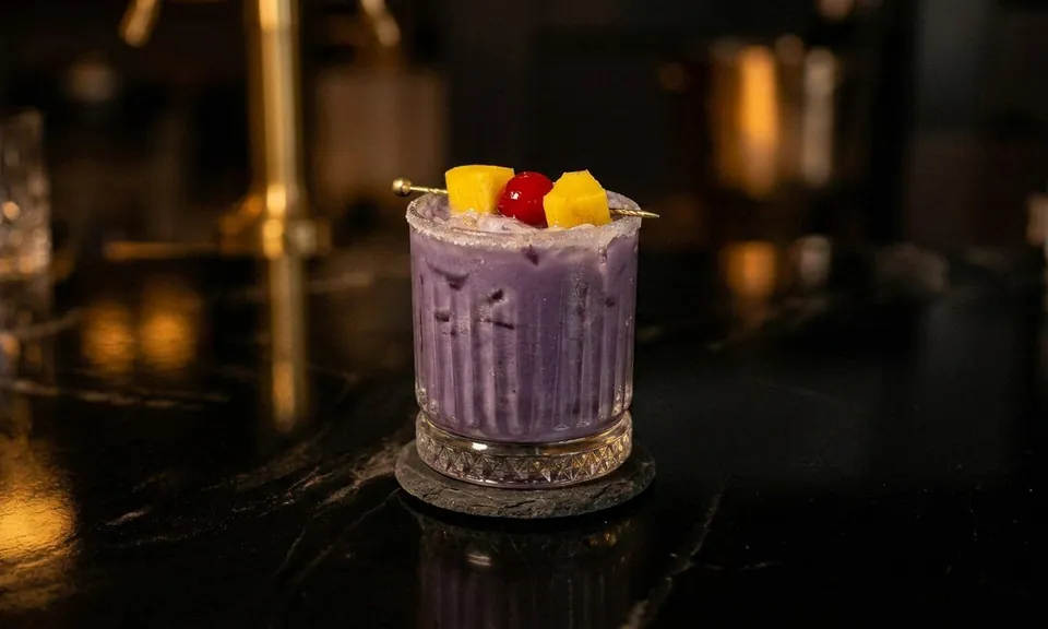 Call Me An Ube, a purple alcohol-free cocktail garnished with pineapple and a cherry, on the bar